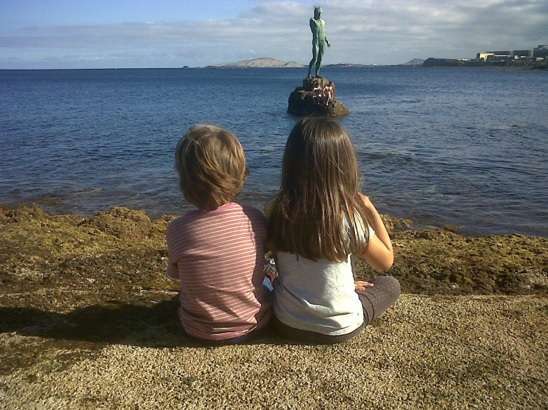Los niños de la pareja argentina mirando la escultura del Neptuno de Melenara (Foto TA)